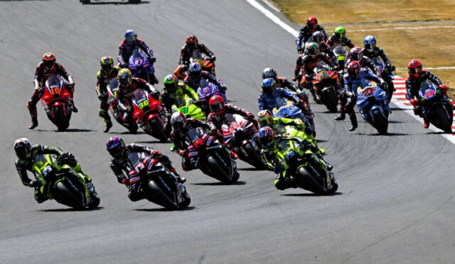Group of motorcycle racers leaning into a sharp turn on a racetrack, wearing bright colorful gear and helmets