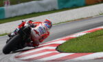 Motorcycle racer in red and white gear leans into a sharp turn on a race track.