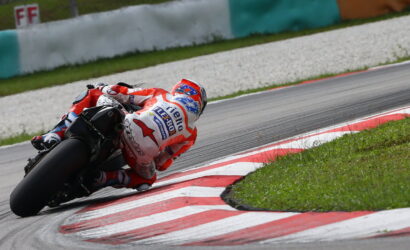 Motorcycle racer in red and white gear leans into a sharp turn on a race track.