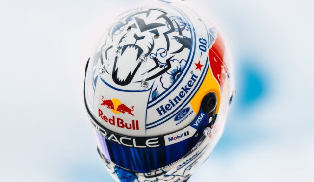 Close-up of a race helmet covered in sponsor logos (Red Bull, Heineken, Oracle) on a white shell with blue and yellow accents, blurred pale background.