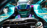 Close-up of a Formula 1 driver in a teal Aston Martin racing car cockpit, helmet with Aston Martin and Bombardier branding