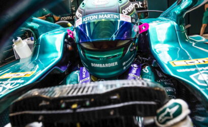 Close-up of a Formula 1 driver in a teal Aston Martin racing car cockpit, helmet with Aston Martin and Bombardier branding