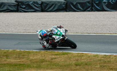 Racer in full leathers and blue helmet leaning into a sharp turn on a race track, bike near horizontal angle