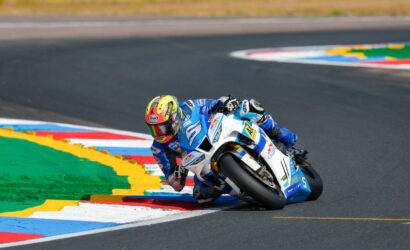 Motorcycle racer in blue and white suit leaning into a sharp turn on a race track, close to colorful curb markings.