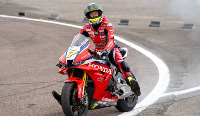 Motorcycle racer in a red Honda racing suit riding a red Honda sportbike on a track, leaning through a curve into the turn.
