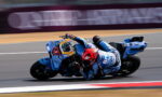 Motorcycle racer in blue-and-white gear leaning hard into a turn on a racetrack.