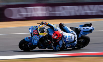 Motorcycle racer in blue-and-white gear leaning hard into a turn on a racetrack.