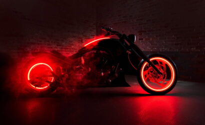 Black motorcycle in a dark brick-walled garage, with red neon rims and underglow lighting.
