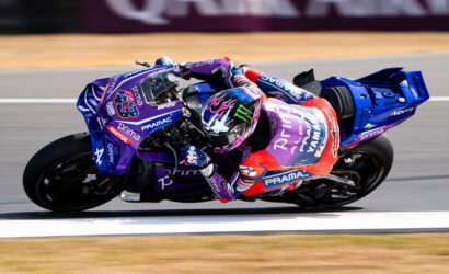 Motorcycle racer in purple Yamaha PRAMAC livery leaning into a high-speed turn on a race track, helmet with flame design.