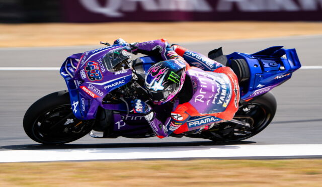 Motorcycle racer in purple Yamaha PRAMAC livery leaning into a high-speed turn on a race track, helmet with flame design.
