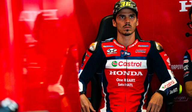 MotoGP rider in a red Honda Castrol racing suit seated in a chair against a red background in the paddock/garage area.