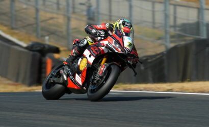 Motorcycle racer in red and white gear leaning into a turn on a race track.