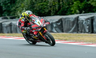 Motorcycle racer in red and black leans into a turn on a race track with red-and-white curbs.