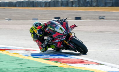 MotoGP rider in neon-green helmet leaning into a sharp turn on a race track with colorful run-off areas behind him.