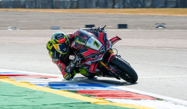 MotoGP rider in neon-green helmet leaning into a sharp turn on a race track with colorful run-off areas behind him.