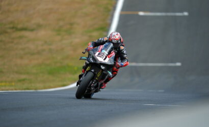 Motorcycle racer leaning into a left-hand turn on a race track in red and black gear.