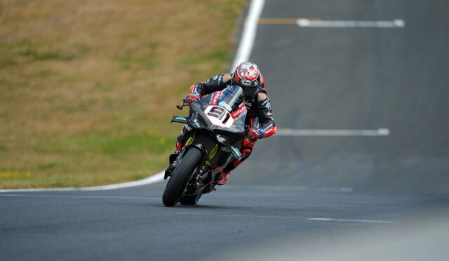 Motorcycle racer leaning into a left-hand turn on a race track in red and black gear.