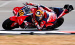 Motorcycle racer on a red Honda bike, number 10, leaning into a corner on a race track.