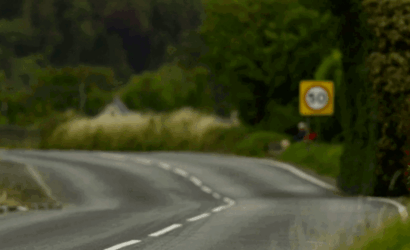 Winding rural road with a dashed center line and a blurred speed limit sign in the distance showing 60 mph.