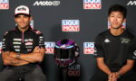 Two MotoGP riders in black team shirts sit with arms folded, a purple and black helmet on a stand between them, in front of a Liqui Moly backdrop.