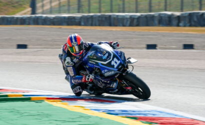 Motorcycle racer in a blue livery leans into a curve on a racetrack, number 31 visible on the bike.