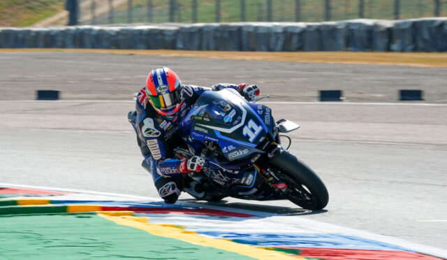 Motorcycle racer in a blue livery leans into a curve on a racetrack, number 31 visible on the bike.