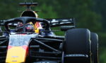 Front view of a Red Bull Racing Formula 1 car with the driver in a colorful helmet behind the halo, on a race track.