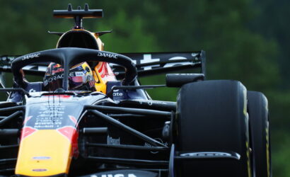 Front view of a Red Bull Racing Formula 1 car with the driver in a colorful helmet behind the halo, on a race track.