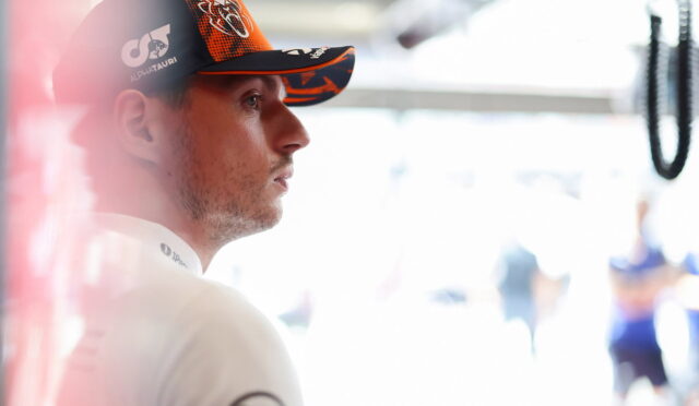 Side profile of a man in a black and orange AlphaTauri cap, looking focused in a bright pit area.