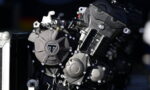 Close-up of a motorcycle engine block with multiple bolts and metal casings, featuring a circular cover with a triangular emblem at the center