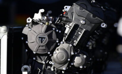Close-up of a motorcycle engine block with multiple bolts and metal casings, featuring a circular cover with a triangular emblem at the center