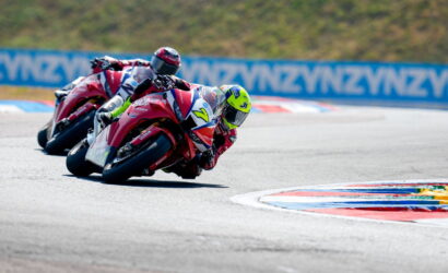 Riders on red motorcycles lean into a sharp turn on a race track, racing in a close group.