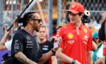 Man with braided hair in a black polo talks to a young Ferrari team member in a red shirt and cap at a gated event behind a crowd of spectators.