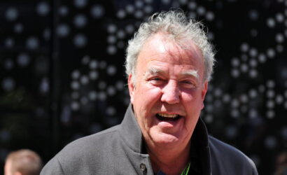 Smiling elderly man with gray hair wearing a gray jacket at an outdoor event.