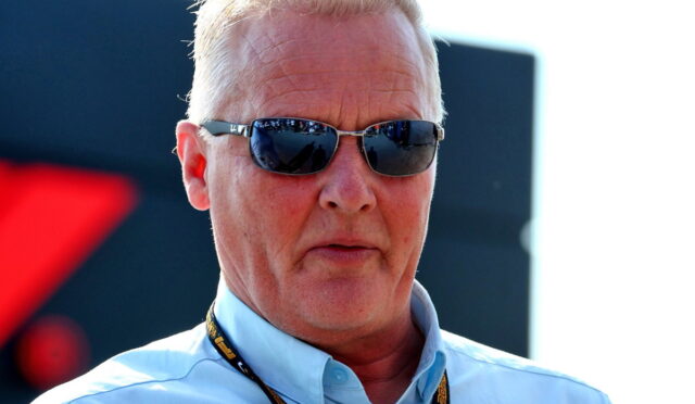 Man wearing a light blue shirt and dark sunglasses at an outdoor event, with a black lanyard around his neck.