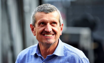 Smiling man in a light blue button-down shirt outdoors, looking to the side.