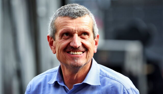 Smiling man in a light blue button-down shirt outdoors, looking to the side.