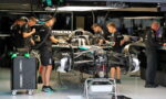 Formula 1 team members in black uniforms working around a race car on a stand in a showroom-style garage.
