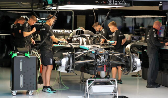 Formula 1 team members in black uniforms working around a race car on a stand in a showroom-style garage.