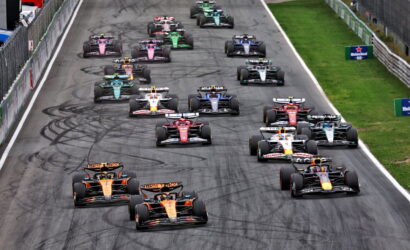 Aerial view of a Formula 1 race start with multiple cars lined up on a track, showing colorful liveries and tire skid marks.