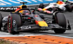 Red Bull Formula 1 car leads around a corner, with orange curbs and a blurred second car behind on the track.
