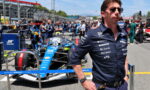 Team member in dark polo and sunglasses in the pit lane with a blue Williams F1 car behind him.