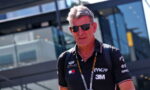 Portrait of a man wearing black polo with logos and sunglasses at an outdoor event, lanyard around his neck