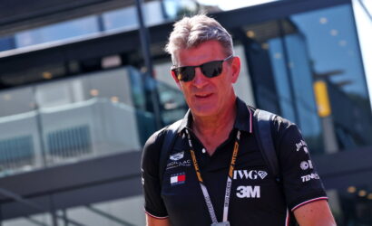 Portrait of a man wearing black polo with logos and sunglasses at an outdoor event, lanyard around his neck