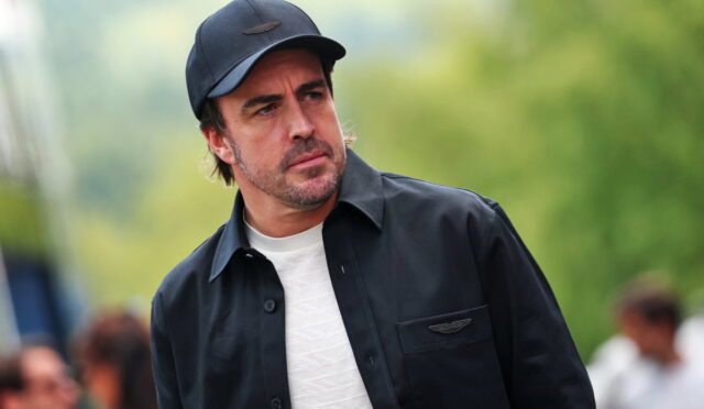 Man in a dark jacket and cap outdoors, looking to the left with a thoughtful expression.