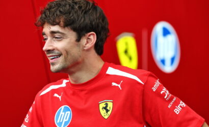 Man in a red Ferrari polo shirt smiling, with sponsor logos visible on the chest and sleeves.