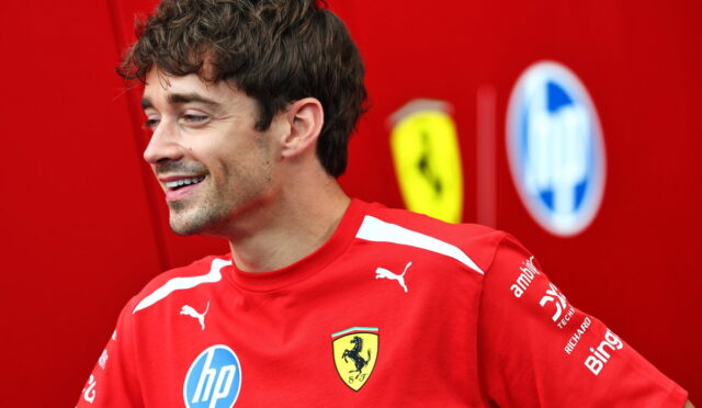 Man in a red Ferrari polo shirt smiling, with sponsor logos visible on the chest and sleeves.