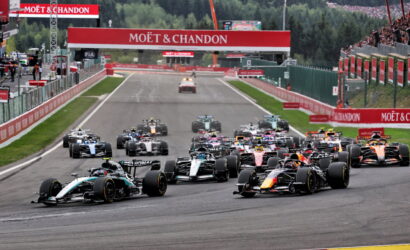 A pack of Formula 1 race cars accelerates off the starting line under red Moët & Chandon banners before a bend.