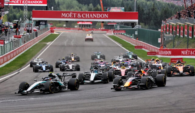 A pack of Formula 1 race cars accelerates off the starting line under red Moët & Chandon banners before a bend.