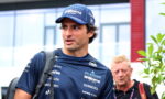 Man in a Williams F1 Team cap and navy polo with sponsor logos, carrying a backpack outdoors and looking to the left.”